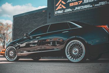 Sleek black luxury sedan parked beside a brick building under a blue sky.
