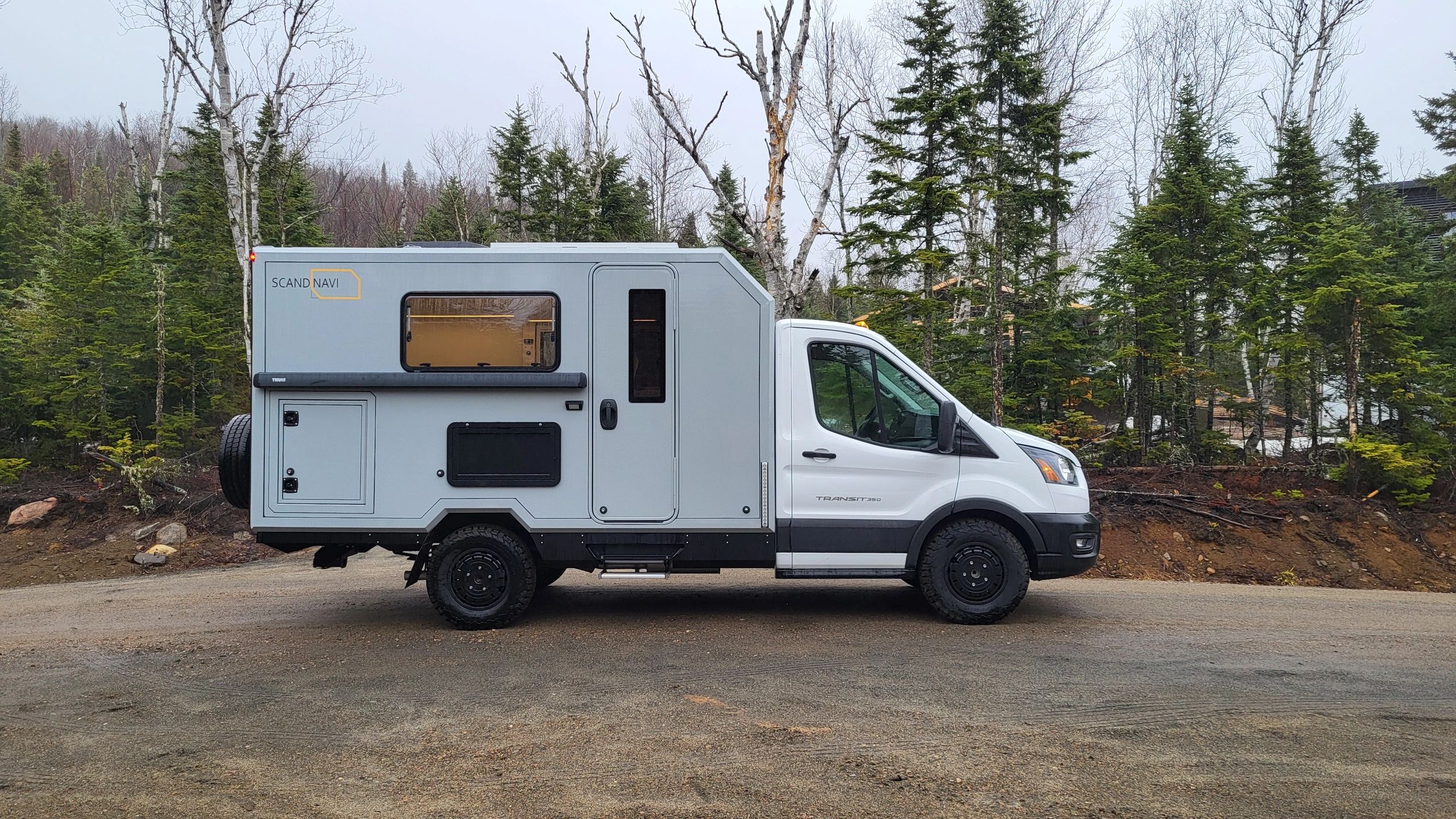 A sleek, modern camper van parked on a forest road.