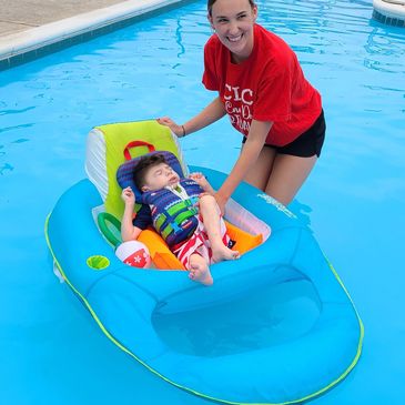 Woman helping baby in pool float.