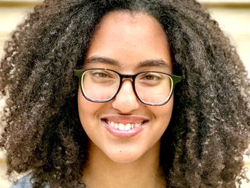 Smiling person with curly hair and glasses.