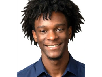 A young man with dreadlocks smiling in a blue shirt.