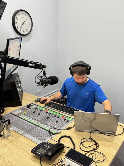 Radio host working at a mixing console with headphones in a studio.