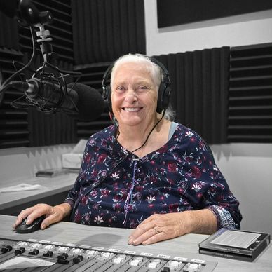Elderly woman smiling in a recording studio with headphones and microphone.