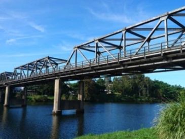 A metal bridge spanning over a calm river under a clear blue sky.