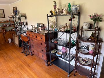 A room with wooden flooring, multiple shelves, and a chest of drawers filled with decorative items.