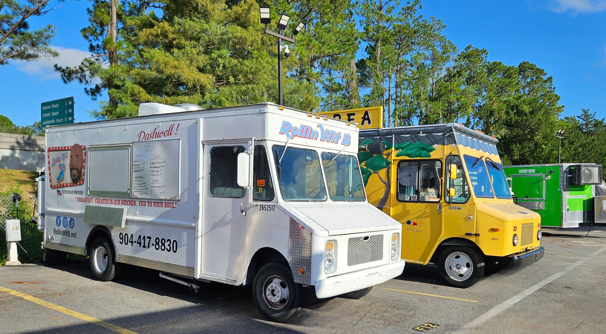 Two colorful food trucks parked side by side under a bright blue sky.