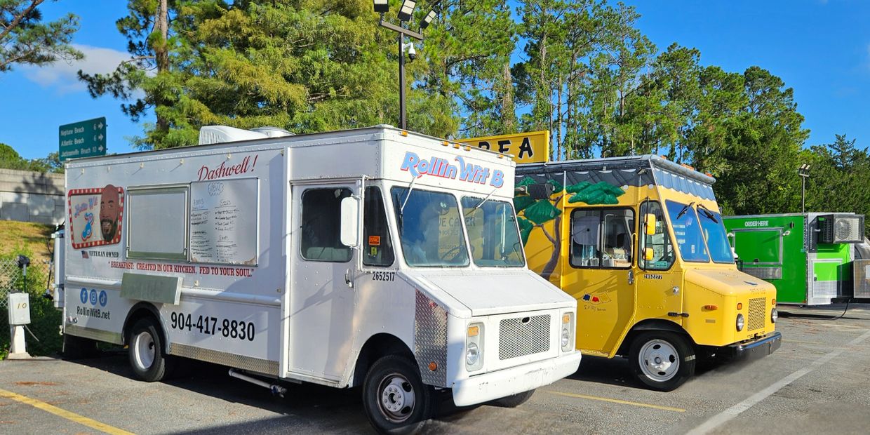 Two colorful food trucks parked side by side under a bright blue sky.