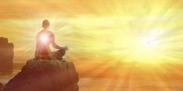 Person meditating on a rock at sunrise with radiant light.