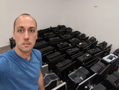 A man, standing in a room filled with black desktop computers, monitors, and keyboards.