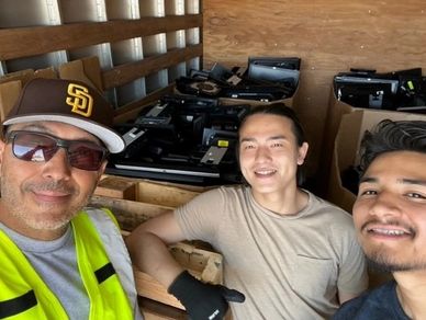 Three smiling men, inside a truck filled with discarded electronic components for recycling.