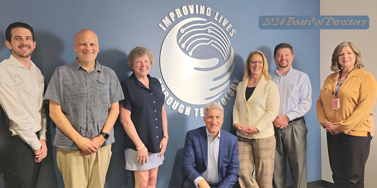 An image of our Board of Directors in front of our Improving Lives Through Technology logo.