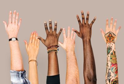 Group of raised hands, black, white, brown, and tatooed.