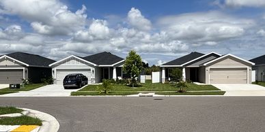 Suburban street with modern houses and a car under a partly cloudy sky.