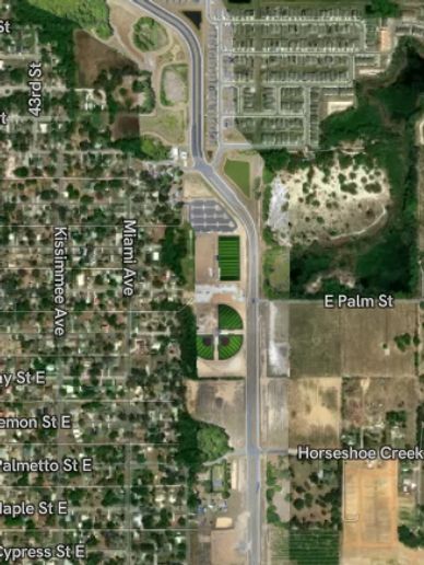 Aerial view of a suburban area with streets, green spaces, and a sports field.