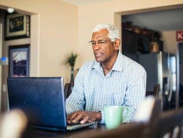Older man focused on laptop work at home.