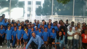 Large group of children and adults posing outdoors, many wearing blue shirts.