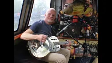 Man playing a metal guitar inside a room with musical equipment.