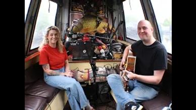 Two people sitting in a cozy boat cabin, one holding a guitar.