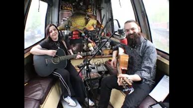 Two musicians playing guitars inside a cozy bus.