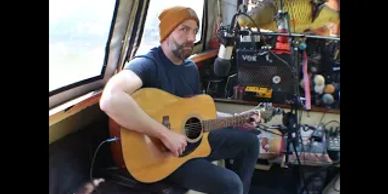 Man playing acoustic guitar inside a cozy room with musical equipment.