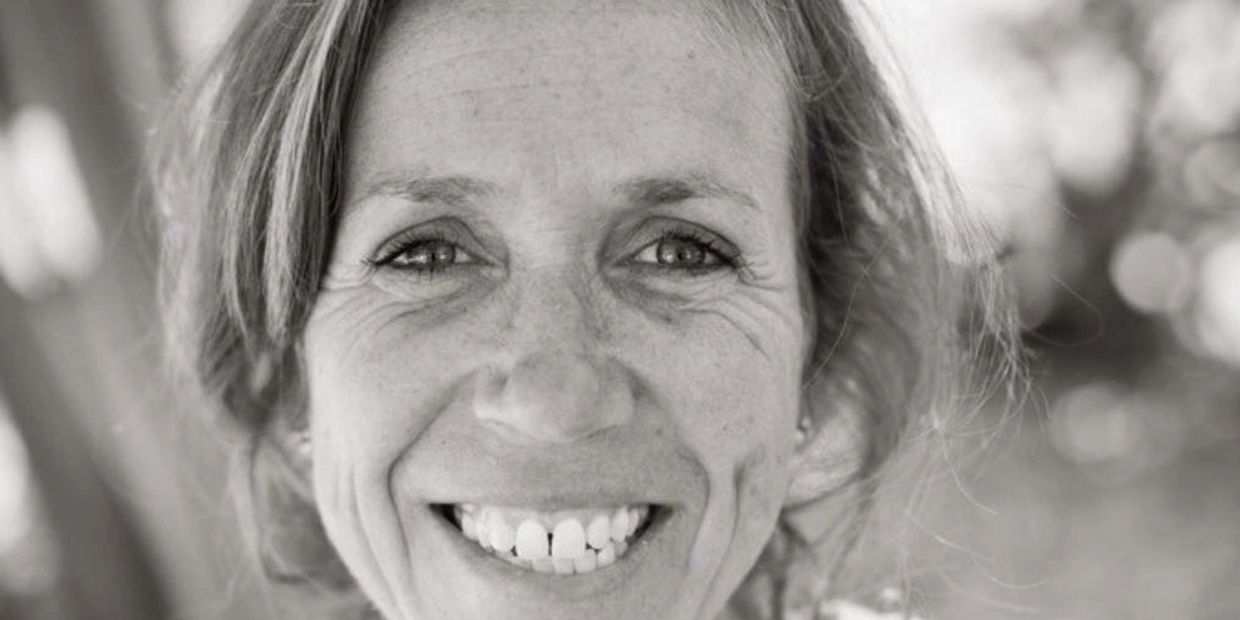 Close-up black and white portrait of a smiling woman with visible wrinkles and natural expression.