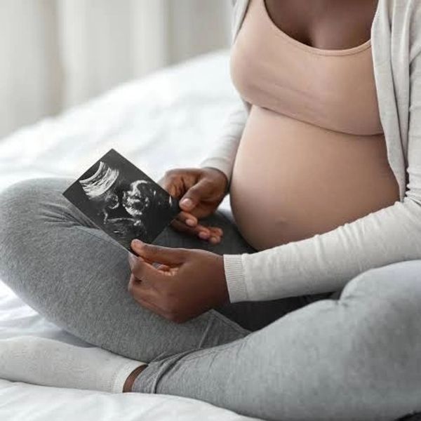 Pregnant woman sitting cross-legged holding an ultrasound image.