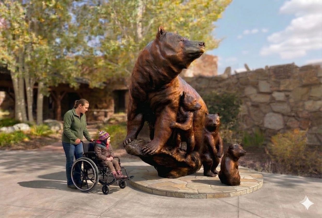 A woman pushes a child in a wheelchair near a large bear family sculpture outdoors.