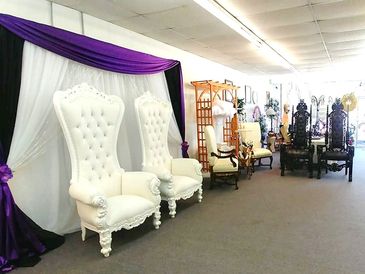 A display of various elegant chairs, including two white throne-like chairs with purple drapes.