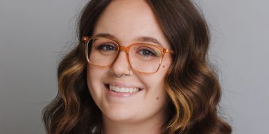 Smiling woman with wavy hair and glasses against a gray background.