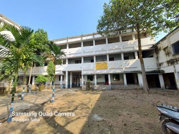 Three-story school building with trees and open courtyard under clear sky.