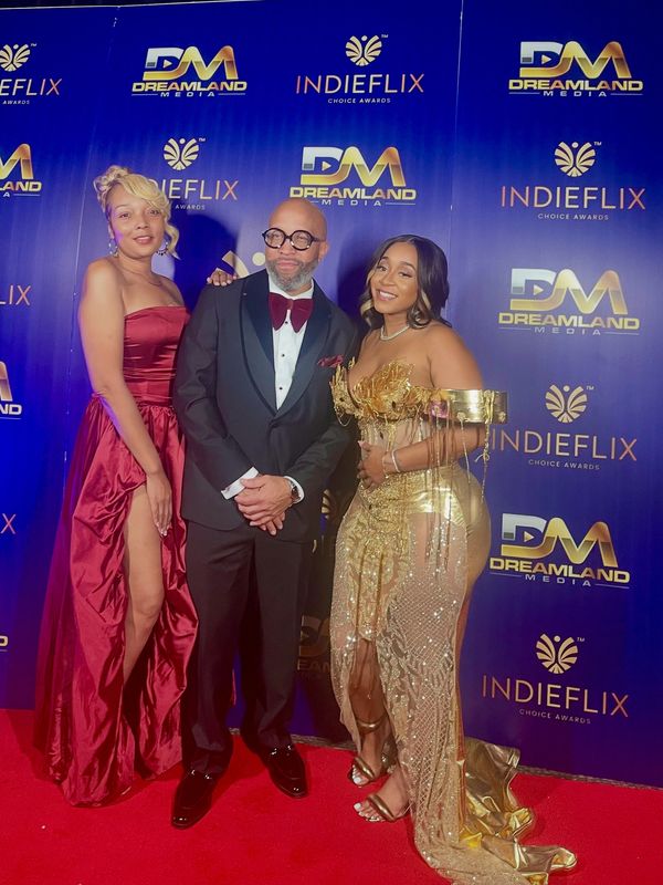 Three elegantly dressed individuals pose on the red carpet at the IndieFlix Choice Awards.