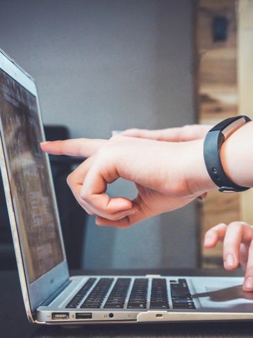 Person pointing at a laptop screen while another types, collaborating on a project.