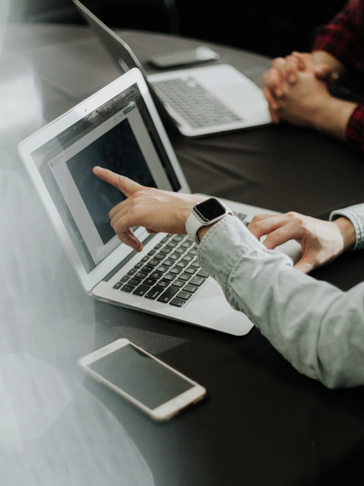 Person pointing at a laptop screen during a meeting, with a smartphone on the table.