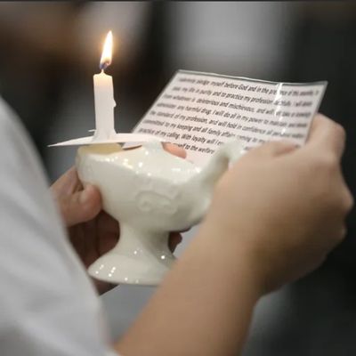 Person holding a candle and reading from a paper.