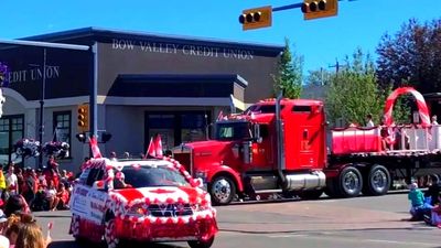 A parade with red and white decorated vehicles passing Bow Valley Credit Union.