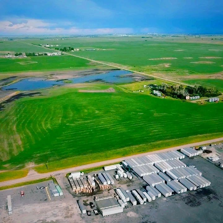 Aerial view of green fields and industrial storage area under a cloudy sky.