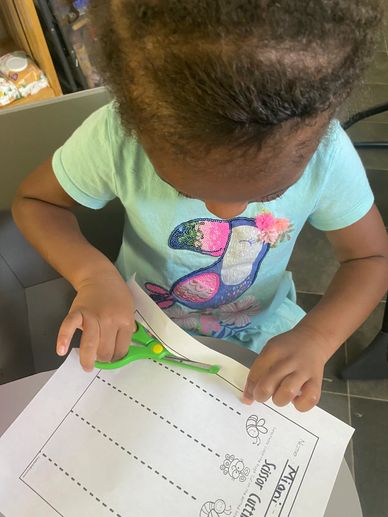 A child cutting paper with green scissors during a craft activity.