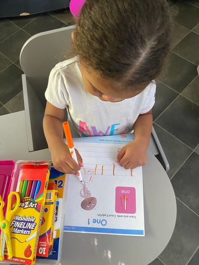 A child coloring and writing on a worksheet with markers at a desk.