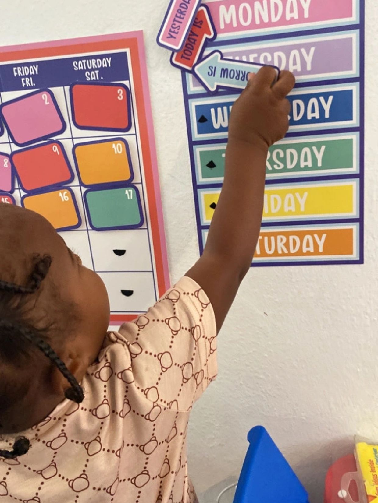 Child learning days of the week and calendar dates on colorful wall charts.