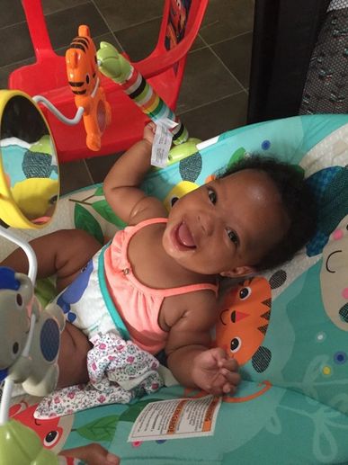 Happy baby smiling in a colorful bouncer with toys.