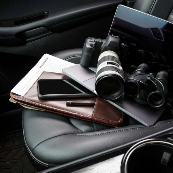 Camera, binoculars, laptop, phone, and documents on a car seat.