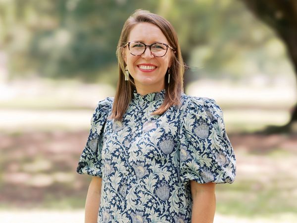 Smiling woman with glasses in a floral dress.