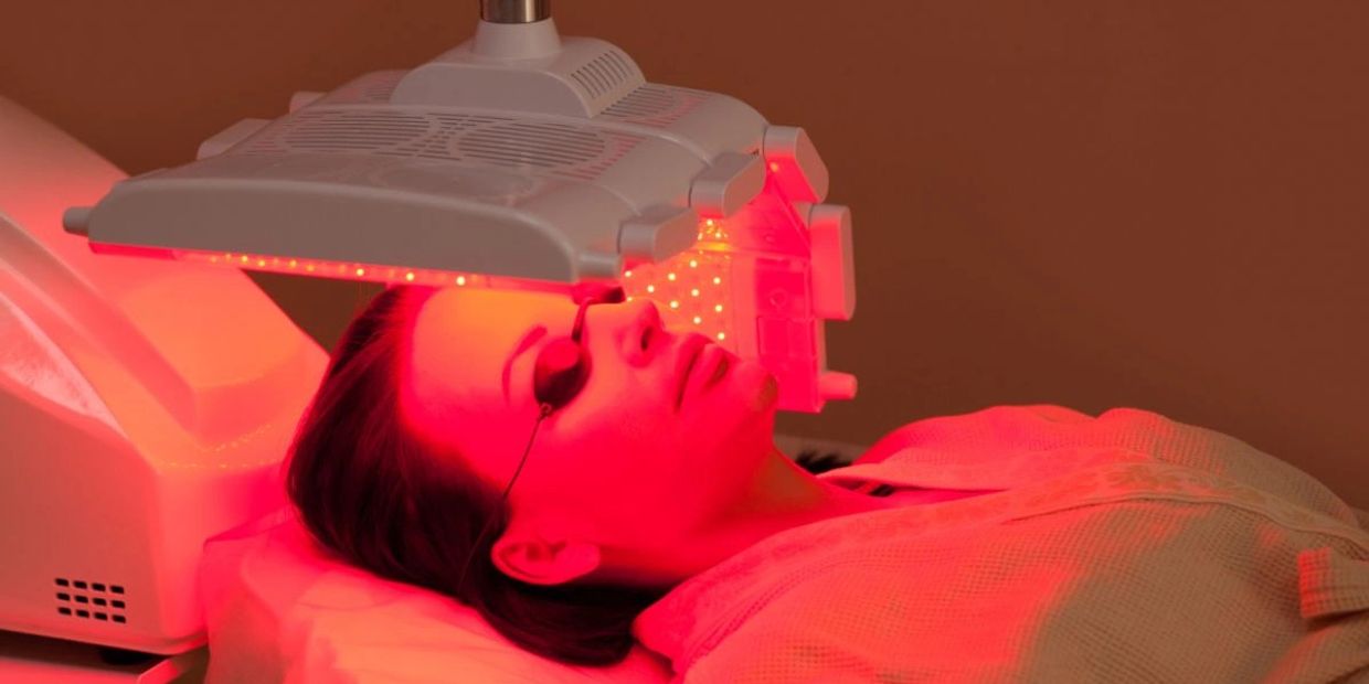 Woman undergoing red light therapy facial treatment wearing protective goggles.