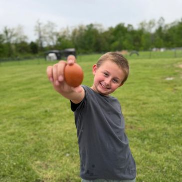 Smiling boy outdoors holding an egg towards the camera.