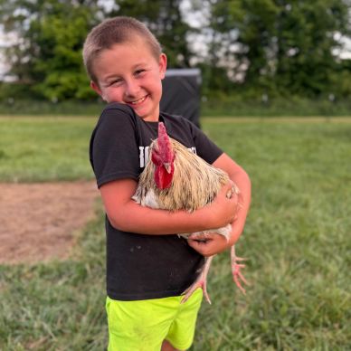 Boy happily holding a chicken outdoors.