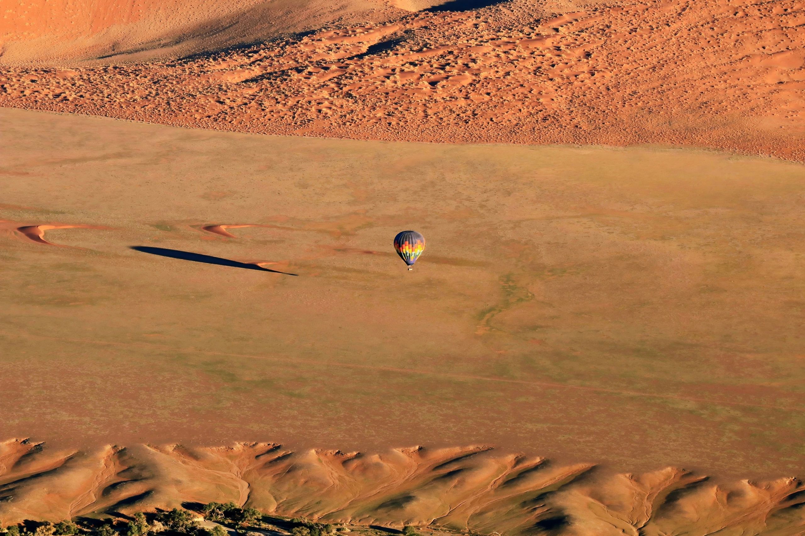 A colorful hot air balloon floats over a vast desert landscape with sand dunes.