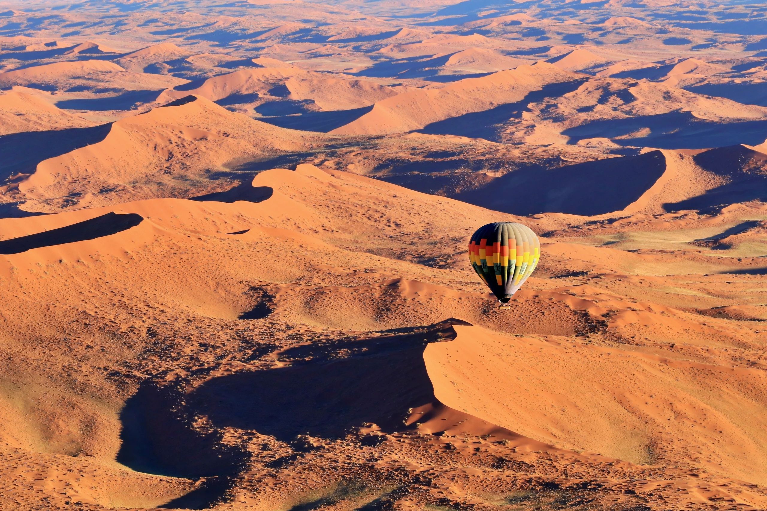 A colorful hot air balloon floats above vast sand dunes in a desert.