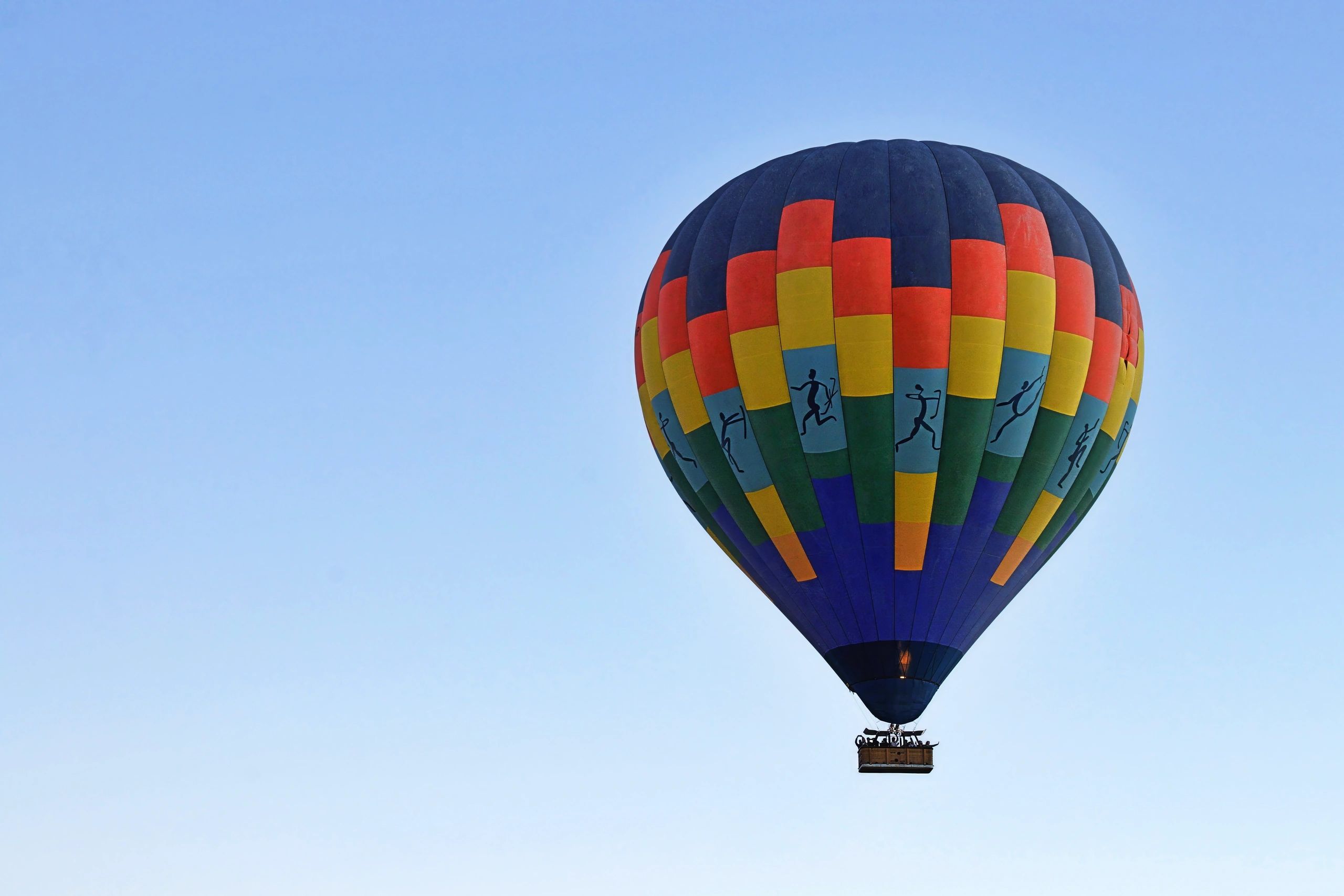Colorful hot air balloon with artistic human figures against a blue sky.