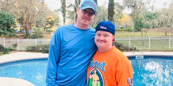 Two men smiling by a backyard pool on a sunny day.