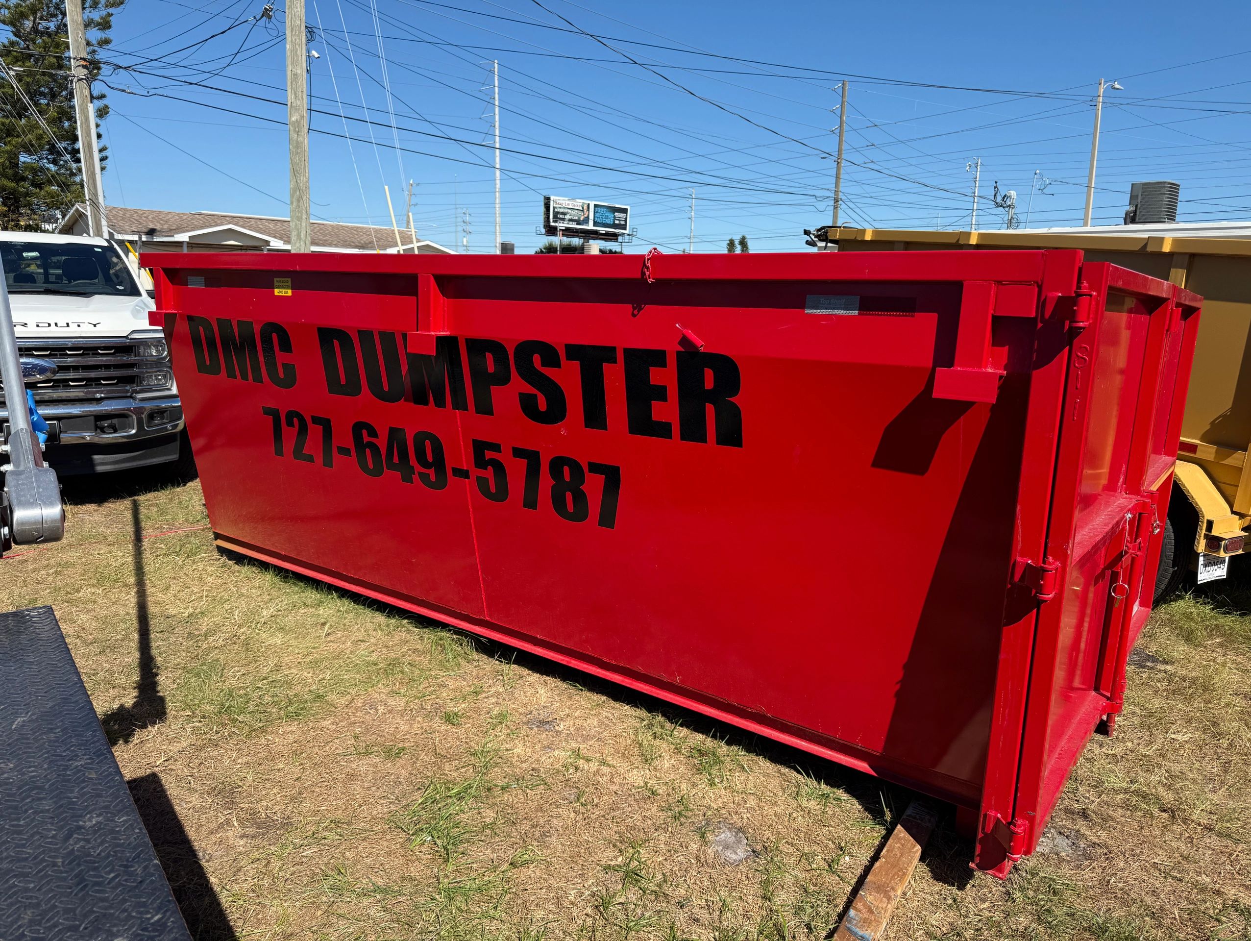 Large red dumpster with contact number and truck in background.